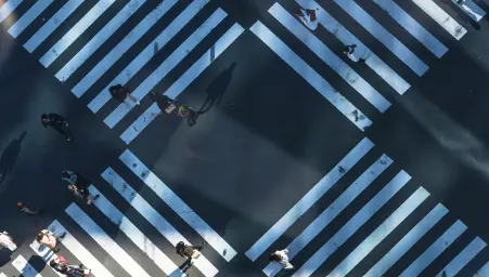 Aerial view of pedestrians crossing a busy intersection with white crosswalk stripes on dark asphalt.